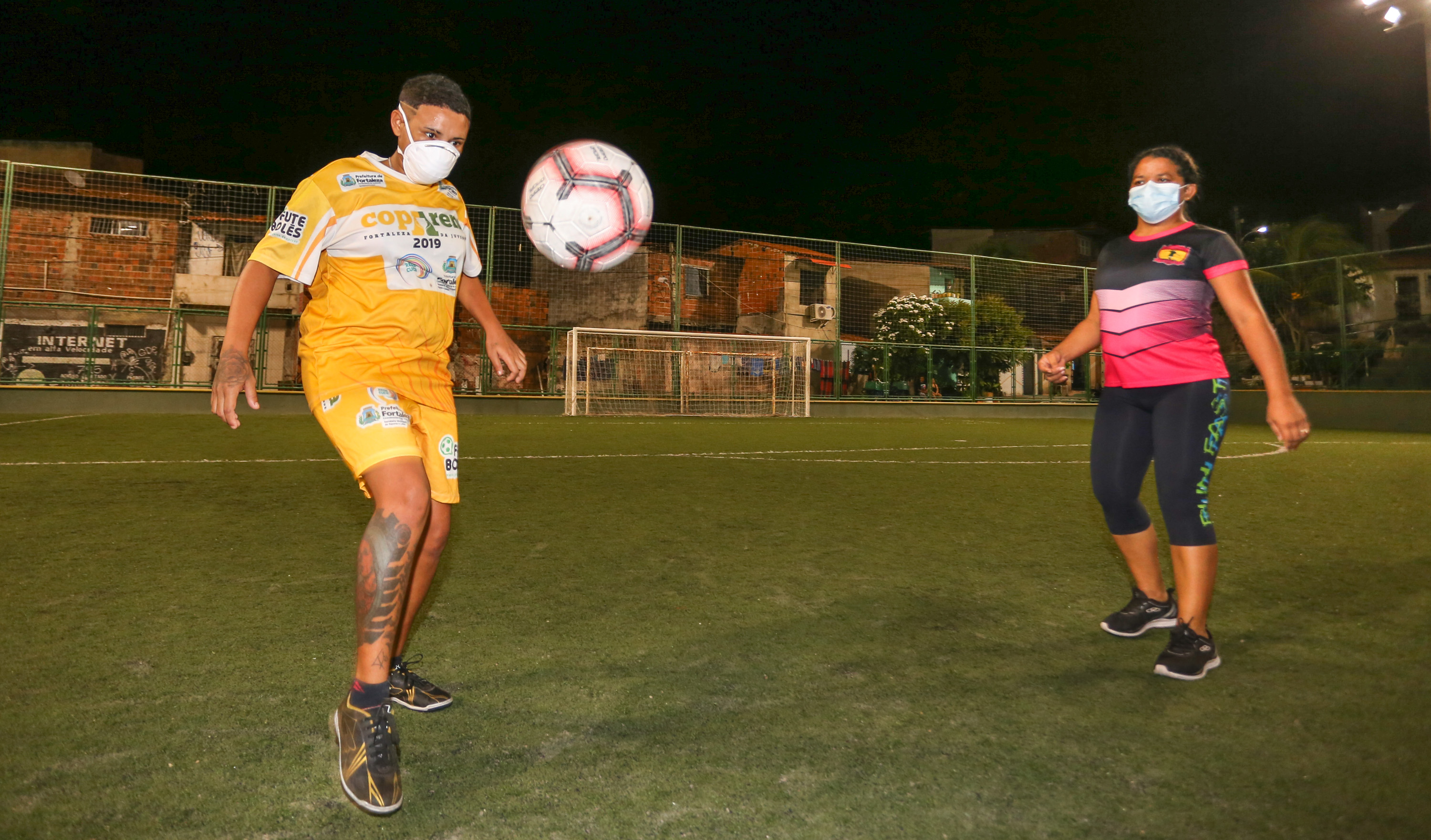 uma mulher faz embaixadinha com uma bola enquanto mulher observa